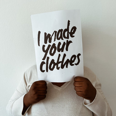 A person of color holding an "I made your clothes" banner in front of his face to raise awareness.