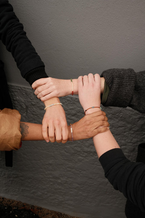 four people wearing Not I But We's mindfulness bracelets and holding each others arms