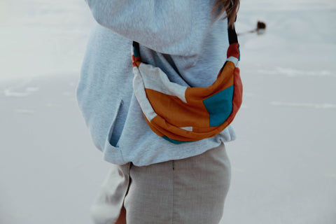 A woman wearing Not I But We's patchwork moonbag at the beach.