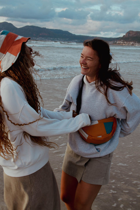 Two woman having fun while wearing Not I But We's patchwork moonbag and bucket hat.