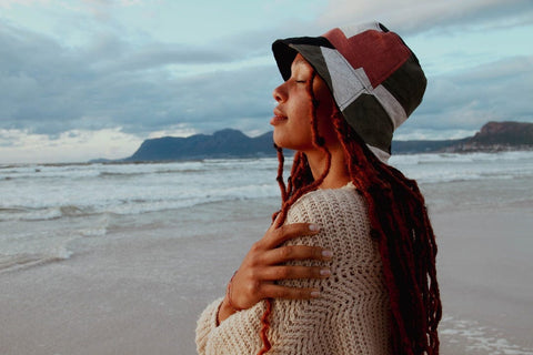 Olive Patchwork Bucket Hat presented by a young woman at the beach.