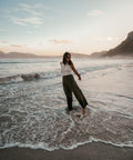 A young woman wearing the olive plisse pants and dipping her feets in the ocean.