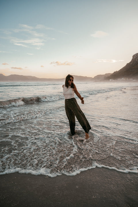 A young woman wearing the olive plisse pants and dipping her feets in the ocean.