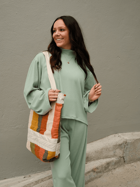 A young woman smiling while wearing the quilted tote bag. 