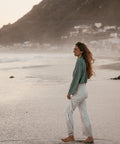 a young woman in a green knit crop sweater at the beach facing the wind