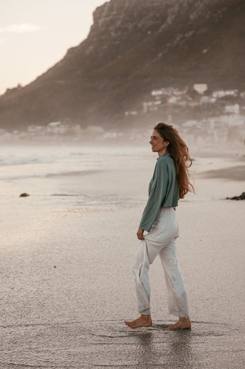 a young woman in a green knit crop sweater at the beach facing the wind